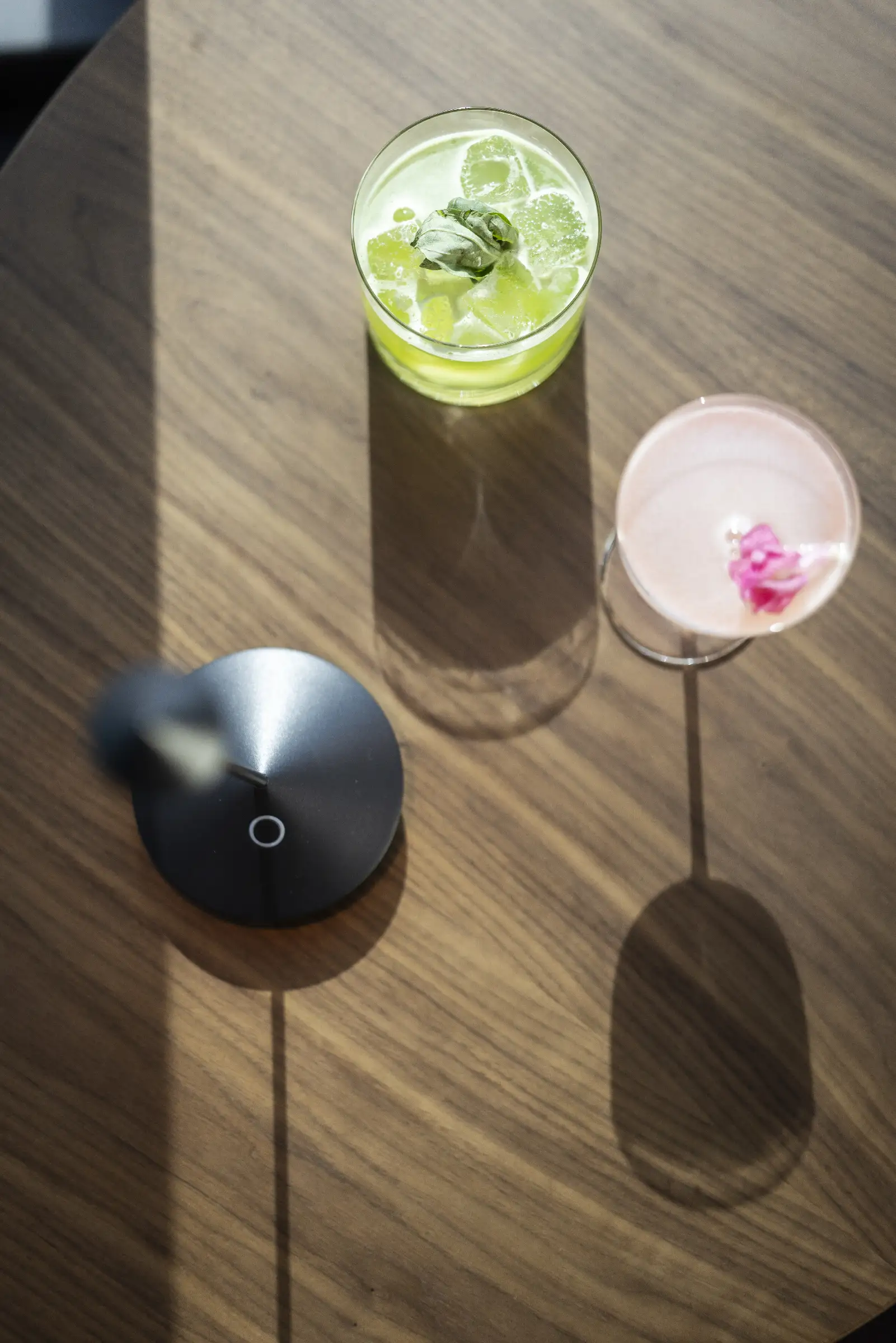 Zwei Cocktails auf einem Holztisch, einer mit Limetten und Minze, der andere mit einer Blüte dekoriert.