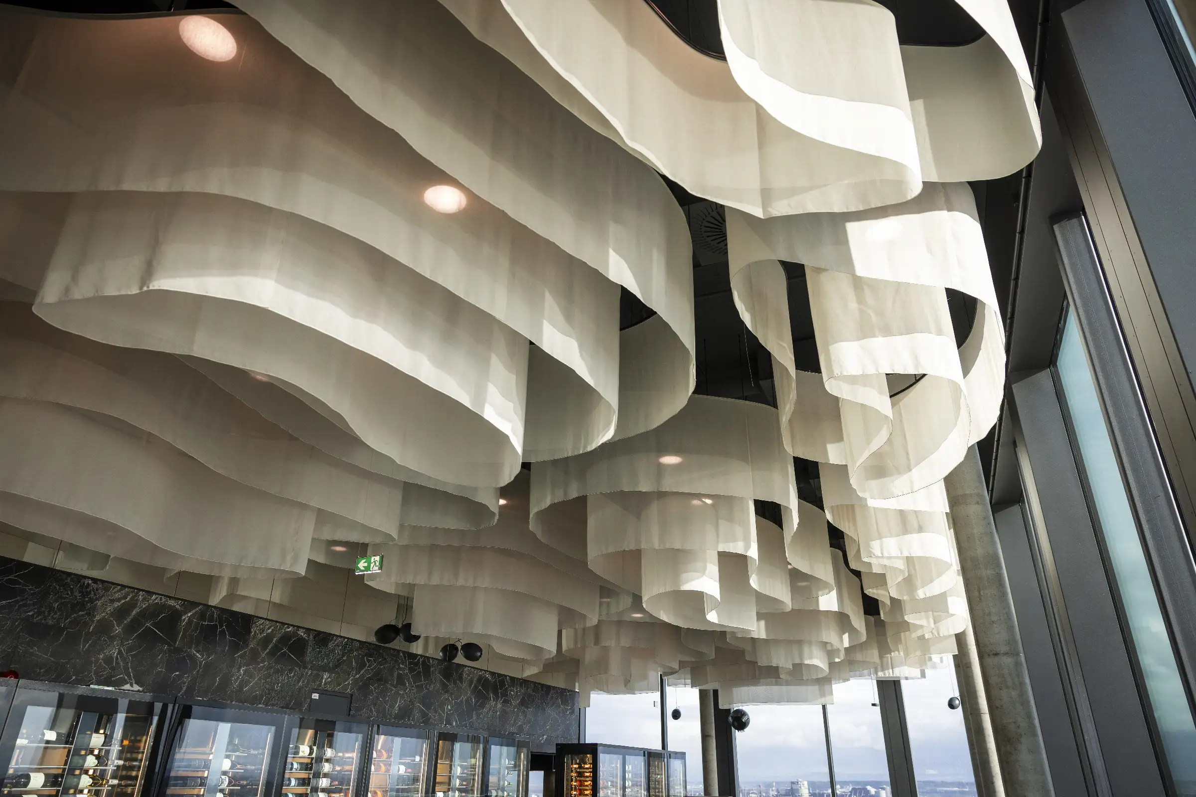 Moderne Deckeninstallation mit geschwungenen Stoffelementen und Beleuchtung im Restaurant Q27.