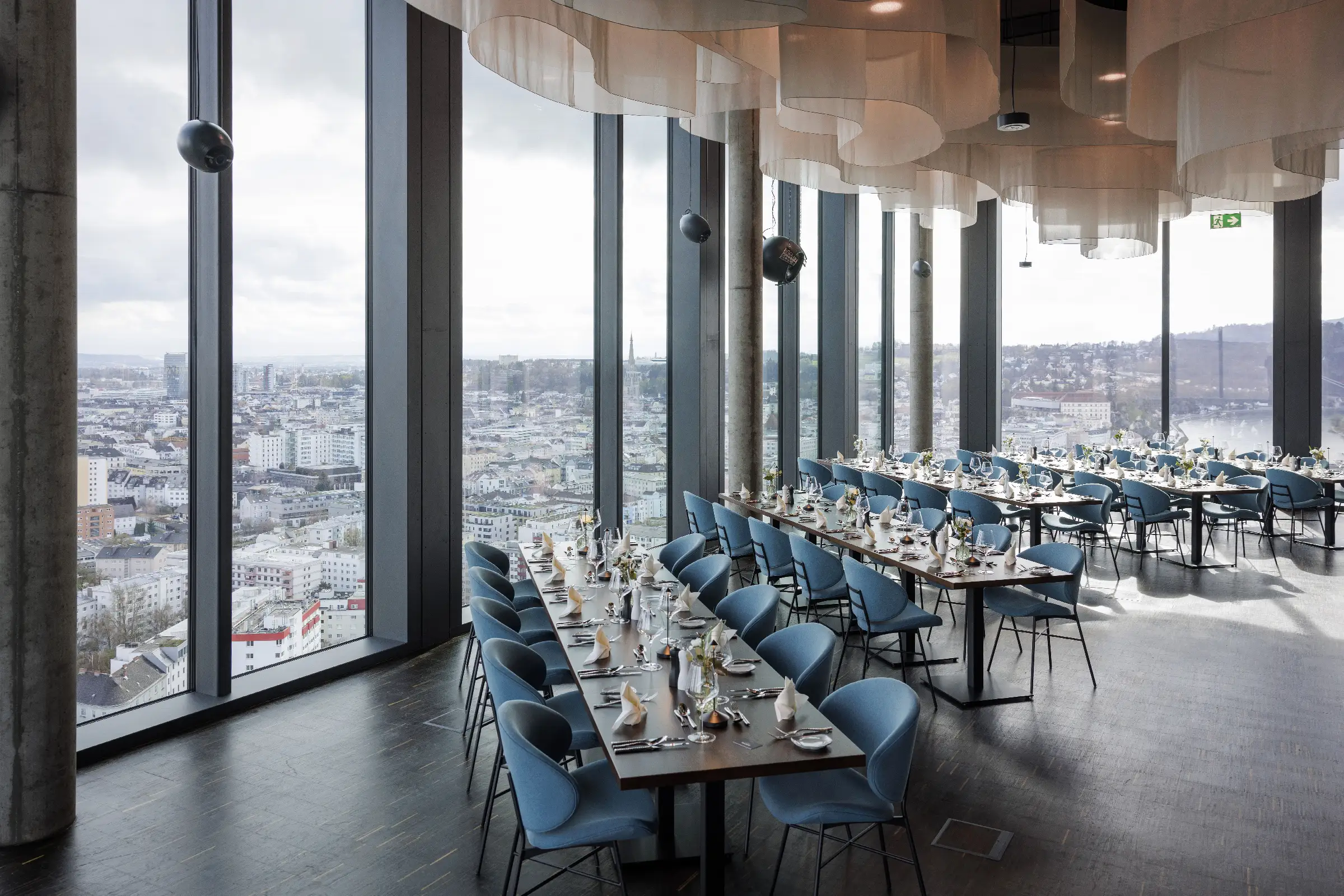 Elegantes Restaurant mit Blick auf die Stadt, stilvoll gedeckte Tische und moderne Einrichtung.