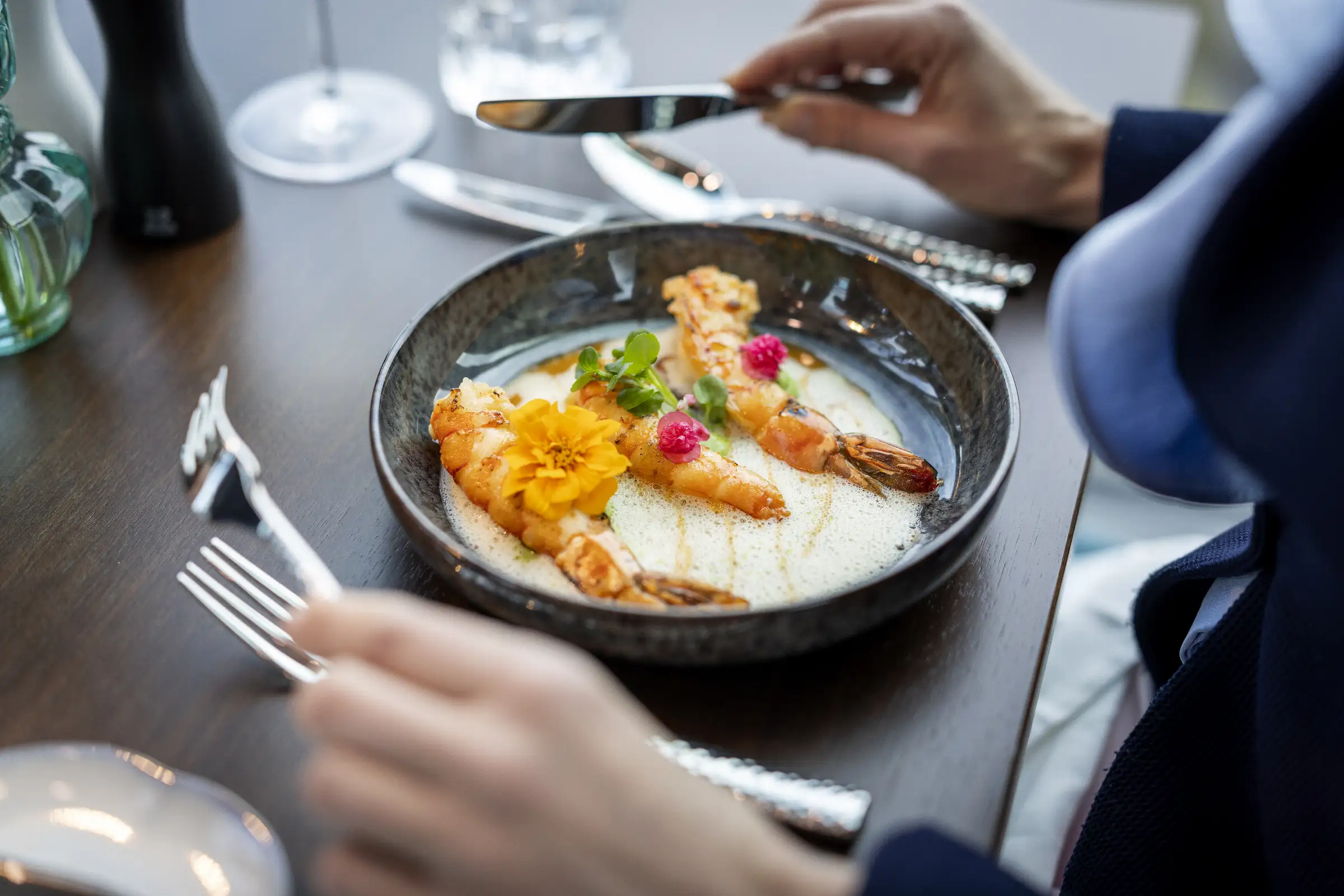 Gegrillte Garnelen mit feiner Sauce und essbaren Blüten auf schwarzem Teller im Restaurant
