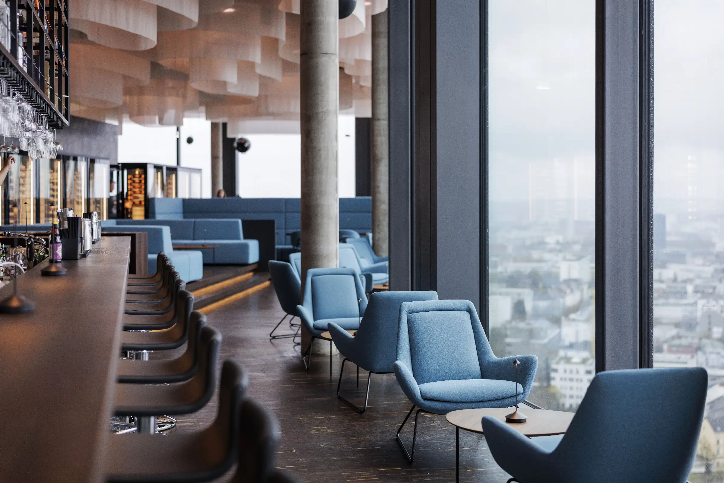Moderne Innenansicht des Restaurants Q27 mit stilvollen blauen Sesseln und Blick auf die Stadt.