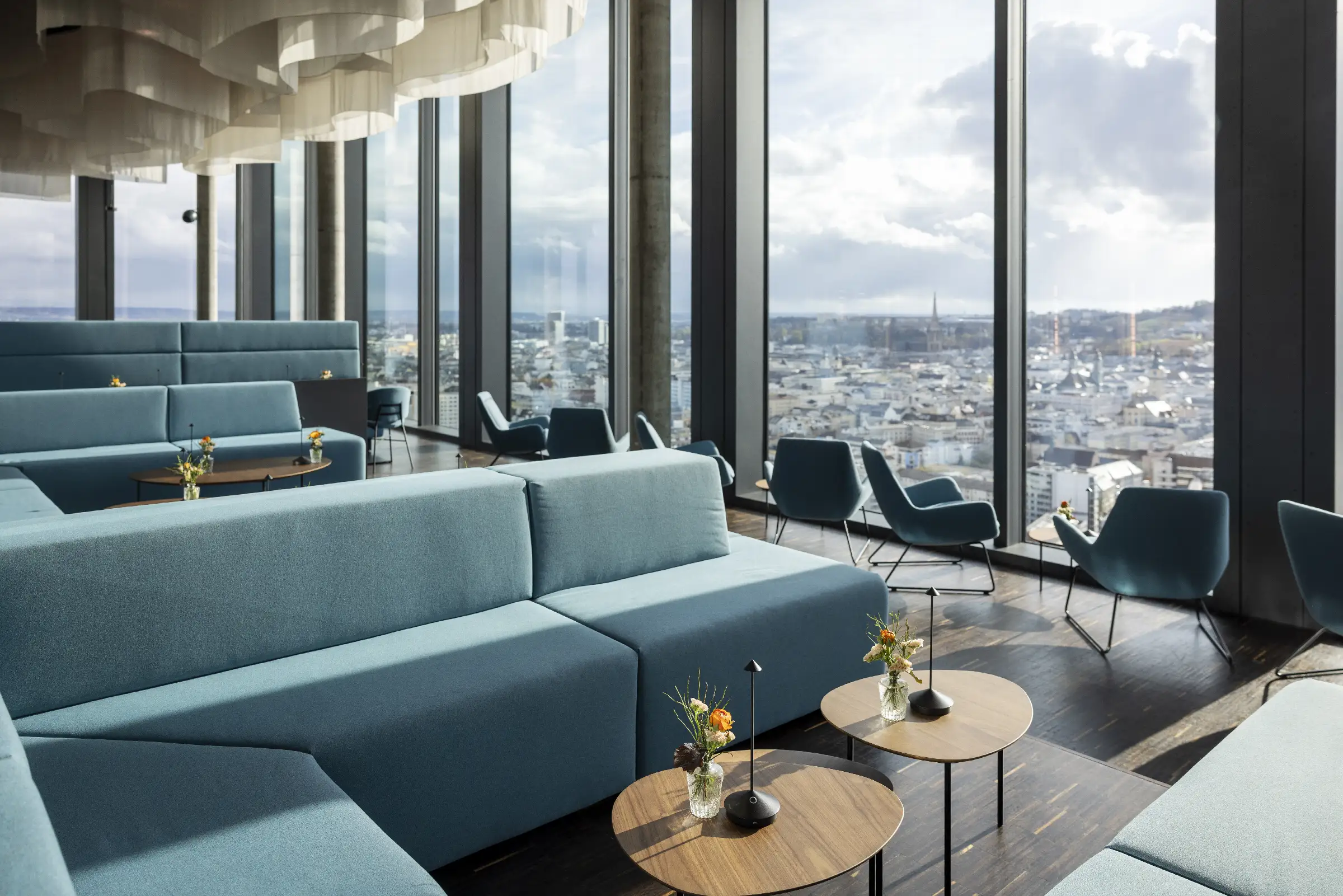 Moderne Lounge mit Blick auf die Stadt, stilvolle Möbel und Blumenarrangements auf Tischen.