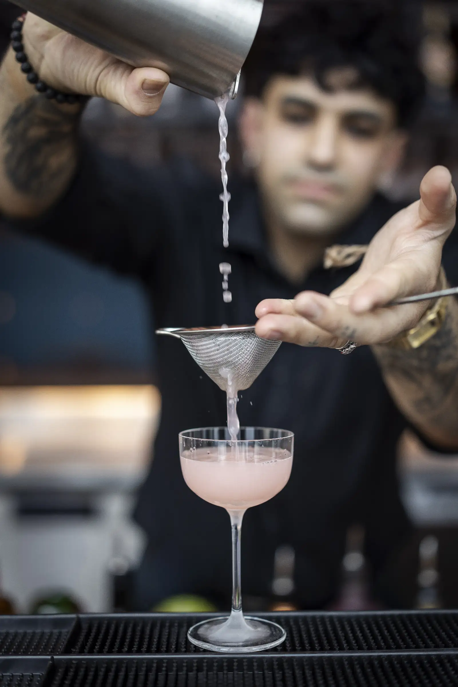 Ein frisch zubereiteter Cocktail wird durch ein Sieb in ein Glas gegossen, serviert an der Bar.